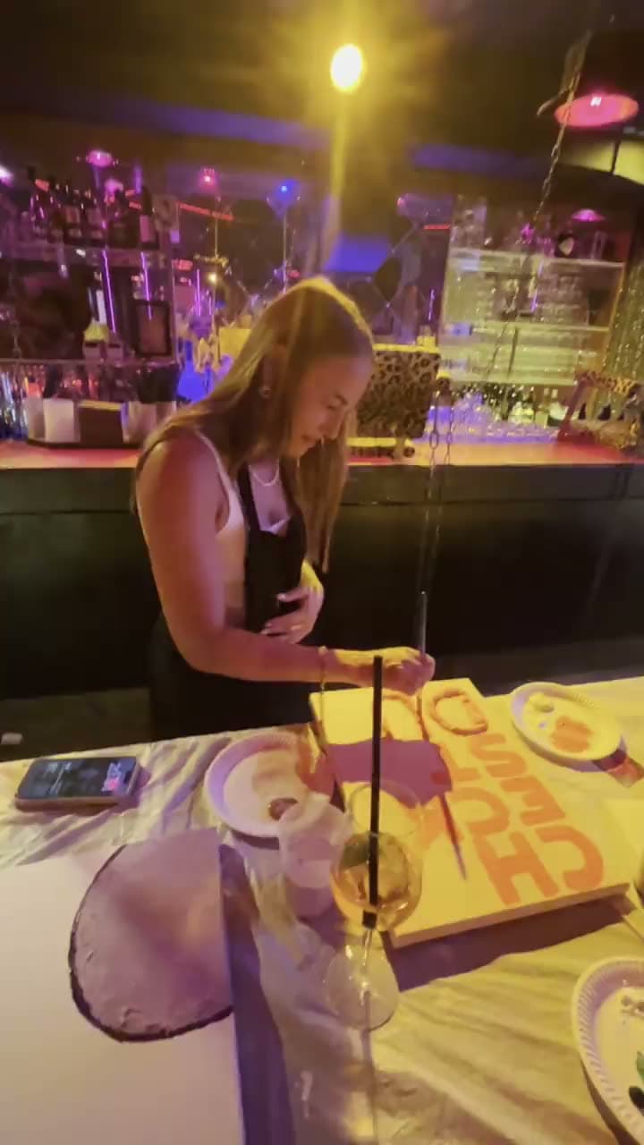 Eine Gästin bemalt eine Leinwand, davor ein Drink, in einer bunten Bar